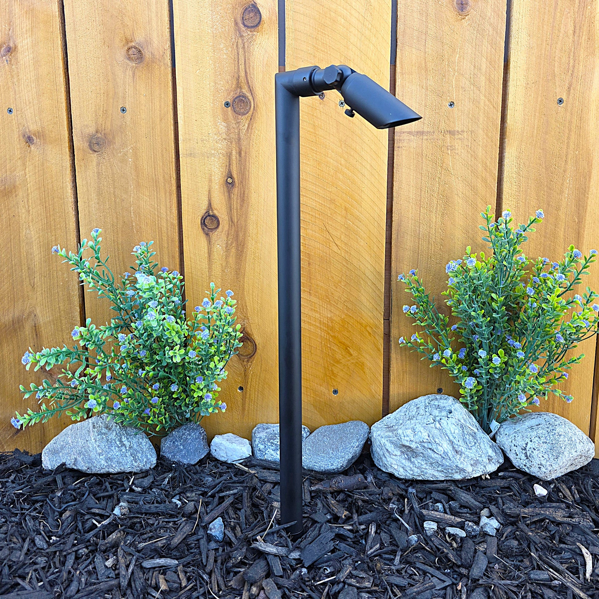 Zone Solid Brass Directional Path Light on a stake beside a wooden fence, delivering focused outdoor illumination.