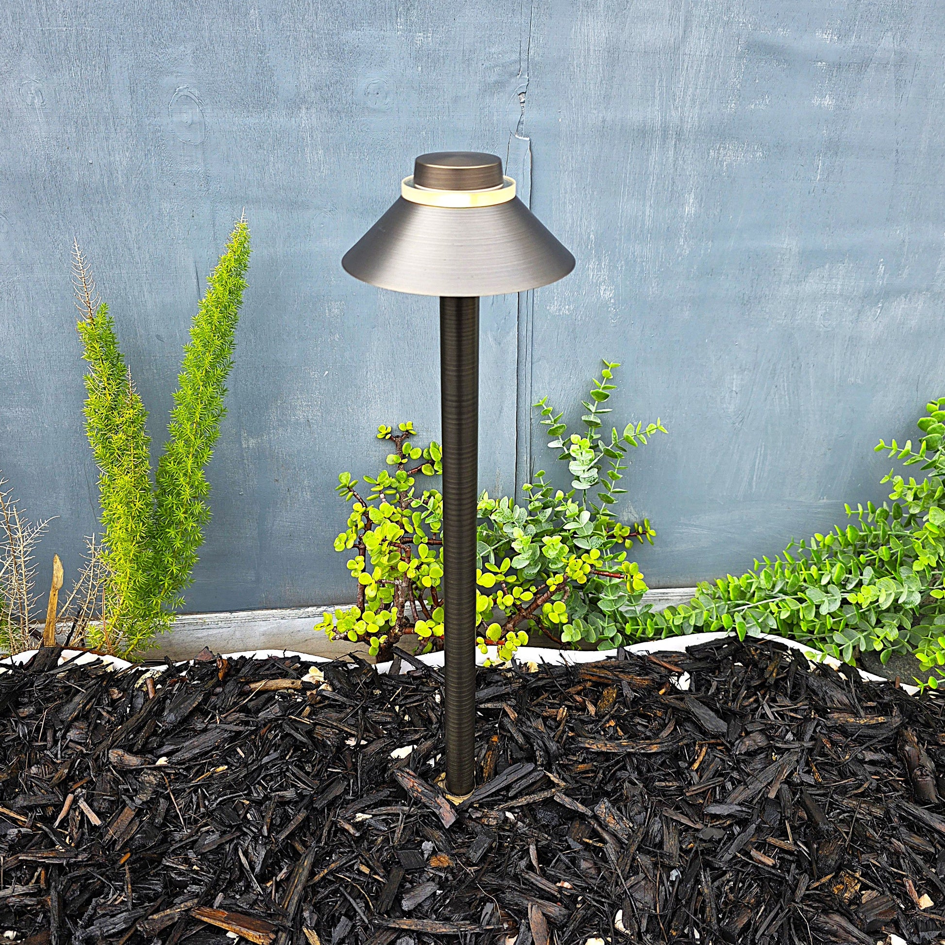 Garden lamp post with plants and mulch against a gray wall