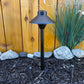 Cascade Cast Brass Path Light outdoor landscape fixture on a garden path beside mulch and rocks near a wooden fence.