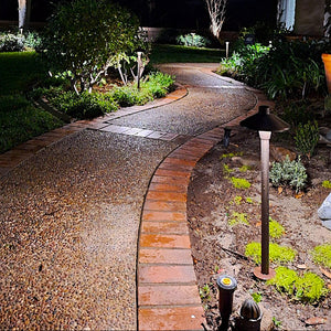 Winding garden path with decorative stones and lighting fixtures in a well-maintained garden.