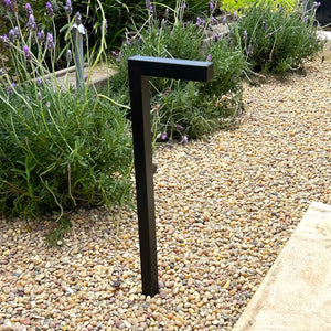 A contemporary pathway light fixture with a sleek gun metal black finish and a clear tempered glass lens, mounted on a stake.